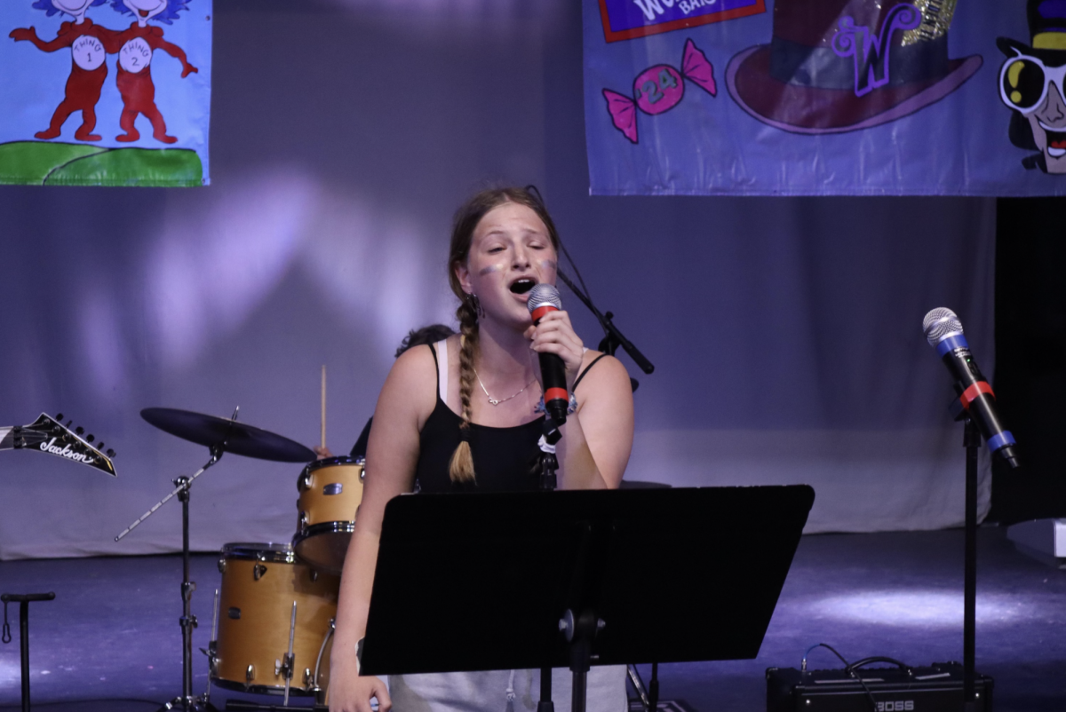 Olivia Broock (‘27) sings into a microphone on stage at Island Lake Camp. Broock found her voice through singing and acting, which has allowed her to express confidence and passion in a world where many women struggle to find outlets to express their opinions and creativity. (Photo courtesy of Olivia Broock)